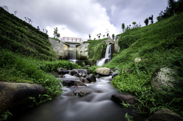 Fototapeta na wymiar beautiful scenery of hidden waterfall with cloudy sky in the middle of tea farm at Cameron Highland, Malaysia.Soft focus and some motion blur due to long exposure. Focus in the center