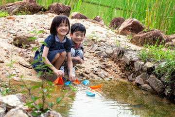 Boy and girl playing paper boats on the river