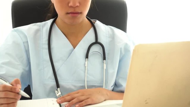 Young asian doctor analyzing medical data at laptop and taking notes