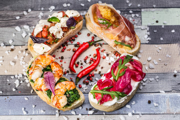 Delicious Canapes.Plate of assorted Italian appetizer bruschetta with chopped vegetables, salmon and meat on ciabatta bread, garnished with green mix salad