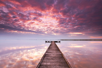 Obraz na płótnie Canvas Licht durchbricht die Wolken, Sonnenaufgang am See mit Steg