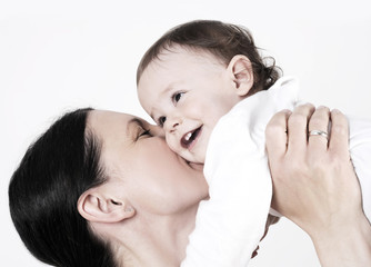 young beautiful mother holding and kissing her cute baby girl , studio shot with light background.