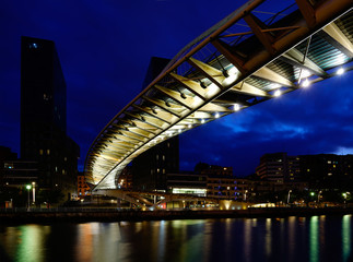 Bilbao, Baskenland in Spanien - Brücke Zubizuri über den Ria del Nervion zur blauen Stunde abends mit Lichtspiegelungen im Wasser