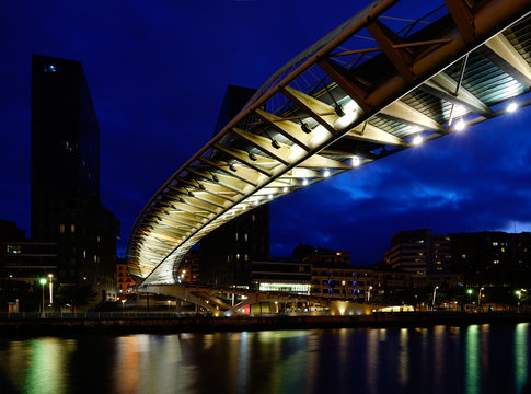 Bilbao, Baskenland in Spanien - Br&uuml;cke Zubizuri &uuml;ber den Ria del Nervion zur blauen Stunde abends mit Lichtspiegelungen im Wasser