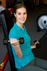 Fototapeta premium The girl holding the dumbbells at the sport club backing smiling 