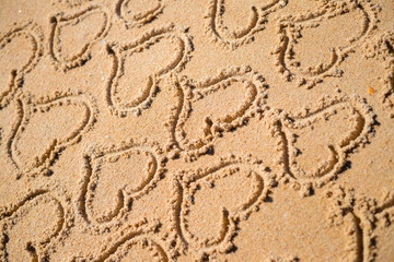Group of many handwritten love heart symbol on sunny sandy beach background. Lovely holiday vacation greeting card.