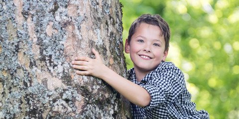 Junge in Karohemd umarmt alten Baumstamm