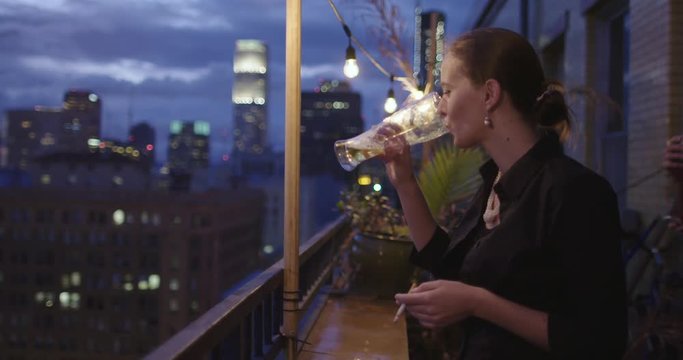Attractive young woman drinking beer from a large glass at a party in front of the night skyline from a balcony in Downtown Los Angeles, California.  Recorded in slow motion at 60fps.