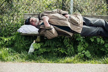 Homeless man sleeping on bench in park.