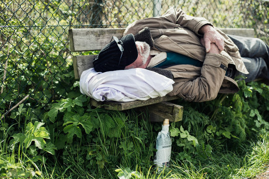 Homeless man sleeping on bench in park.