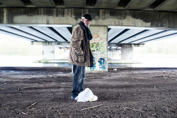 Lost homeless man standing with bag under bridge.