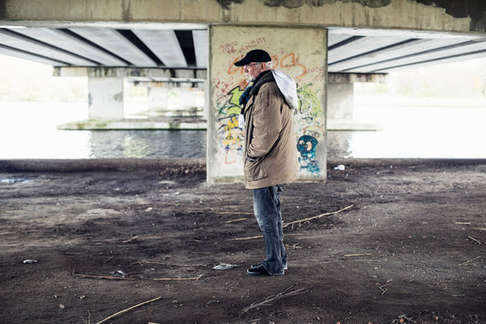Homeless senior man with bag standing under bridge.