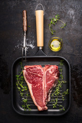 T-bone Steak on frying grill pan with meat fork, oil and seasoning on dark rustic background , top...