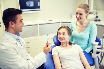 Obraz premium happy dentist showing toothbrush to patient girl