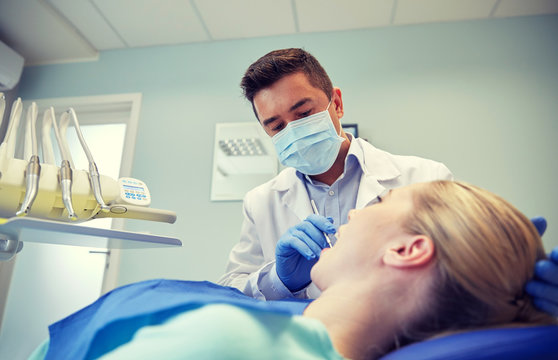 male dentist in mask checking female patient teeth