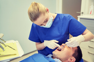 Obraz na płótnie Canvas female dentist checking up male patient teeth