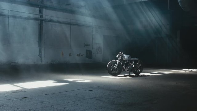 Wide dolly shot of a custom built cafe racer motorcycle standing in the large warehouse garage. 60 FPS slow motion Blackmagic URSA Mini RAW graded footage