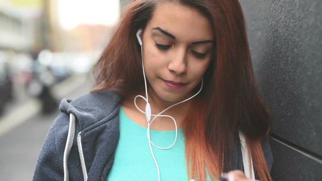 Half length of young handsome caucasian reddish woman listening music with earphones and smartphone handhold, moving her head in step with music – music, relaxing, technology concept