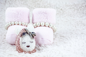 Pink babys bootees with several bracelets and one brooch on the white fur