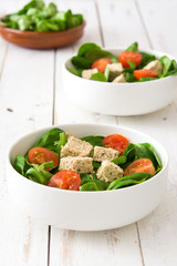 Vegan tofu salad with tomatoes and lamb's lettuce on white wood

