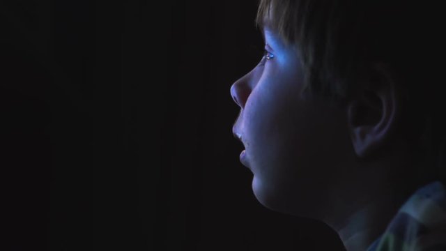 Young boy watching cartoons in a dark room on a computer
