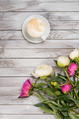 A bouquet of peonies and cup of coffee on a light wooden background. Top view.