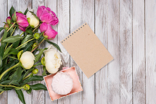 A bouquet of peonies flowers, marshmallow, notebook on white wooden background. Space for text. Top view.