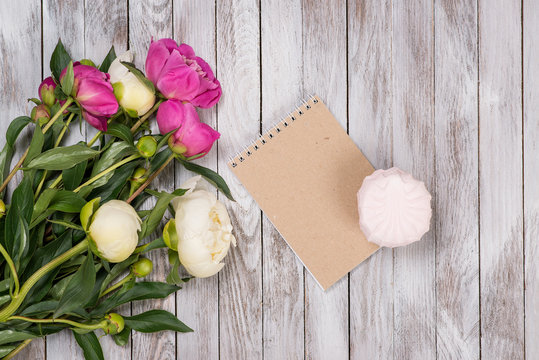 A bouquet of peonies flowers, marshmallow, notebook on the white wooden background. Space for text. Top view.