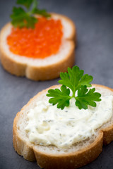 Bread with fresh cream cheese and red caviar on table.