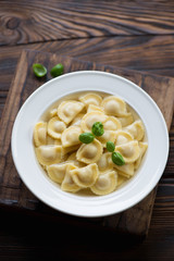 Ravioli in bouillon with green basil, rustic wooden background