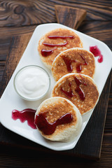 Curd pancakes with sour cream and jam served on a glass plate