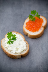 Bread with fresh cream cheese and red caviar on table.