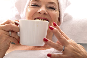 Starsza kobieta pije kawę z białego kubka 