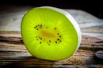 Closeup of green kiwi slice glowing with translucent light on rough wooden surface