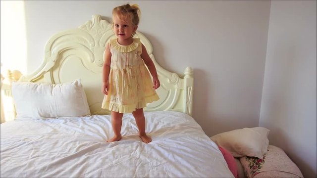 Little Girl Claps Hands Jumps down Bed to Pillows on Floor