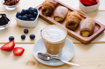 Beautiful  breakfast. Glass cup of coffee with milk served with crushed chocolate, different pastries, berries and raisins on the wooden background.