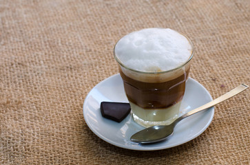 Glass cup of coffee with condensed milk and chocolate on sacking background with copyspace.