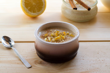 Homemade rice pudding in a ceramic bowl with sticks of cinnamon and lemon on wooden background. Delicious healthy dessert.