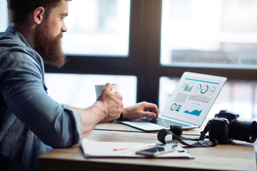 Pleasant bearded man working on the laptop   