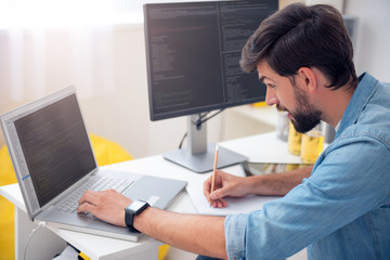 Man looking at laptop and taking notes