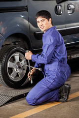 Fototapeta na wymiar Confident Mechanic Fixing Car Tire At Garage