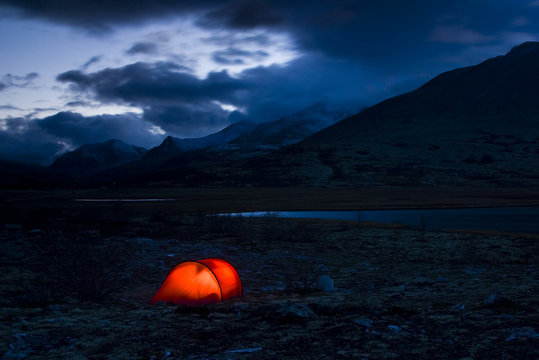 A well-lit red tent at a fjeld massif, Rondane National Park, Norway.
