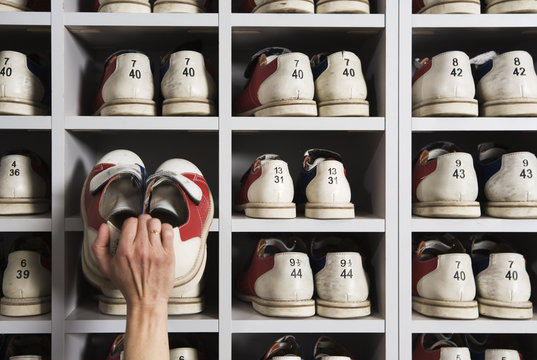 Hand picking shoes on shelves in a bowling alley.