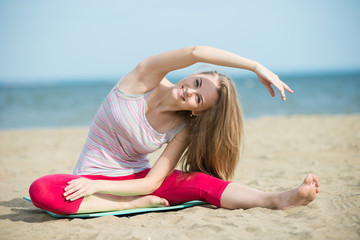 Fototapeta na wymiar Young lady practicing yoga. Beautiful woman posing at the summer sand beach. Workout near ocean sea coast. Beautiful fit tan girl. Fitness model caucasian ethnicity outdoors. Weight loss exercise