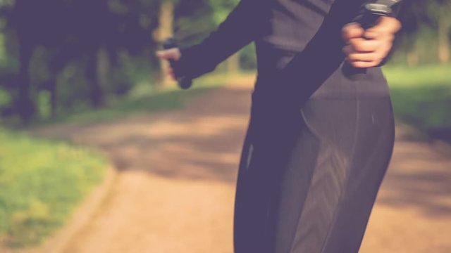Close-up of hands an jumping women on the jump rope. Outdoor sports. Girl jumping on a skipping rope in park path with a green grass on background.. 4K 3840 x 2160 ultra high definition footage