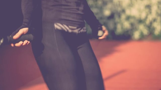 Close-up of hands an jumping women on the jump rope. Outdoor sports. Girl jumping on a skipping rope on on athletic field. Flower busch on background. 4K 3840 x 2160 ultra high definition footage