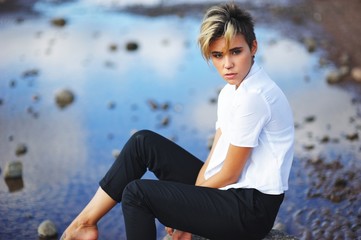 woman in a white shirt and black pants sitting on stone amongst water