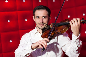 Young musician playing the violin in a restaurant on a red wall.