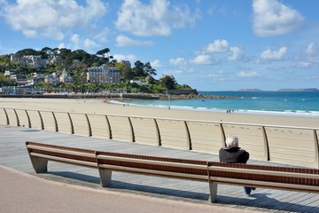 Un retraité assis sur un banc face à la mer et la plage de Perros-Guirec en Bretagne