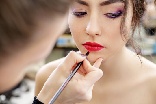 Stylist makes professional lips makeup. Red lips and brush. Beautiful model.